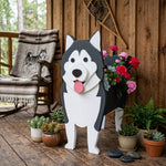 Alaska malamute shaped dog planter stand on a wooden deck with plants and flowers