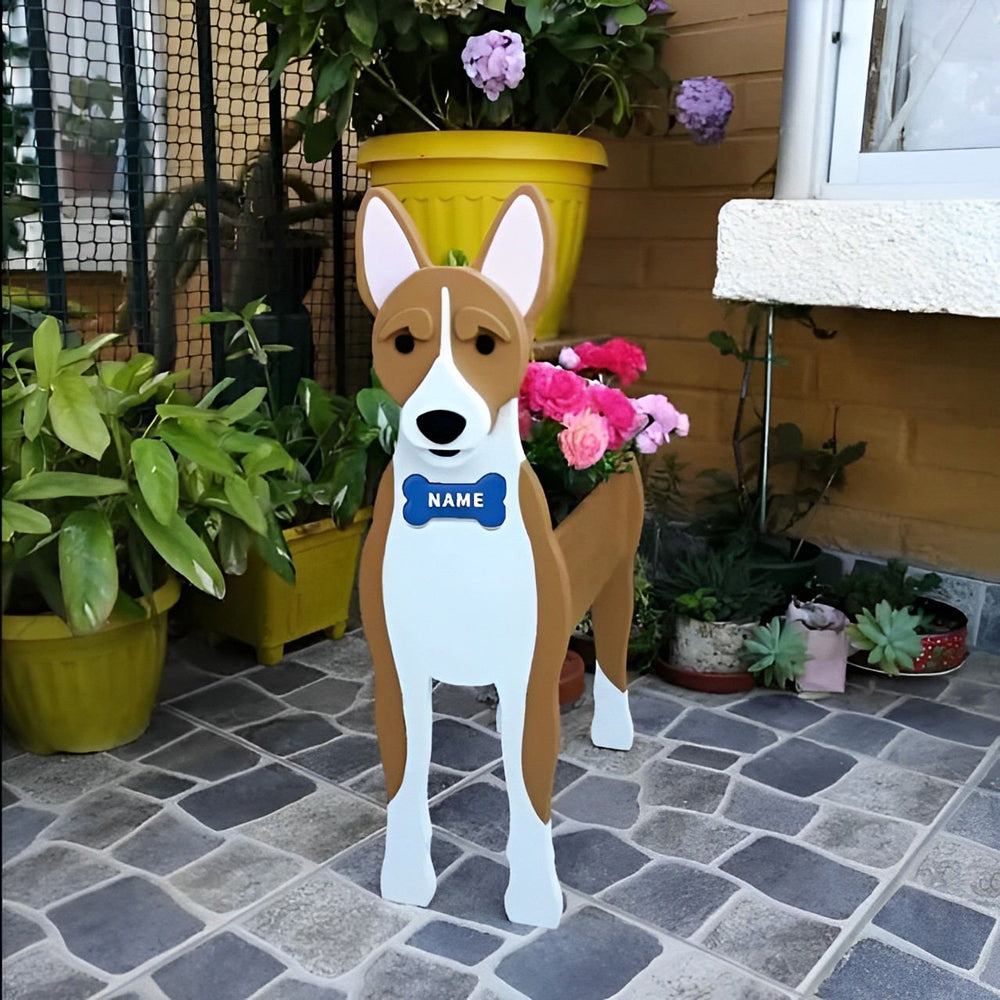 Basenji-shaped dog planter with a blue name tag on a stone patio surrounded by potted plants