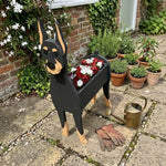 Doberman dog planter filled with fresh flowers is placed in the garden.