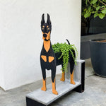 Doberman dog planter filled with fresh flowers is placed in the garden.