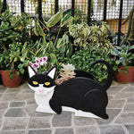 Lying cats planter filled with fresh flowers is placed in the garden