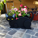 Lying cats planter filled with fresh flowers is placed in the garden