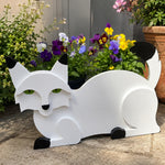 Lying cats planter filled with fresh flowers is placed in the garden