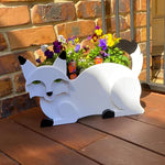 Lying cats planter filled with fresh flowers is placed in the garden