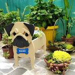 Fawn pug dog planter with a 'NAME' tag surrounded by potted plants on a stone surface
